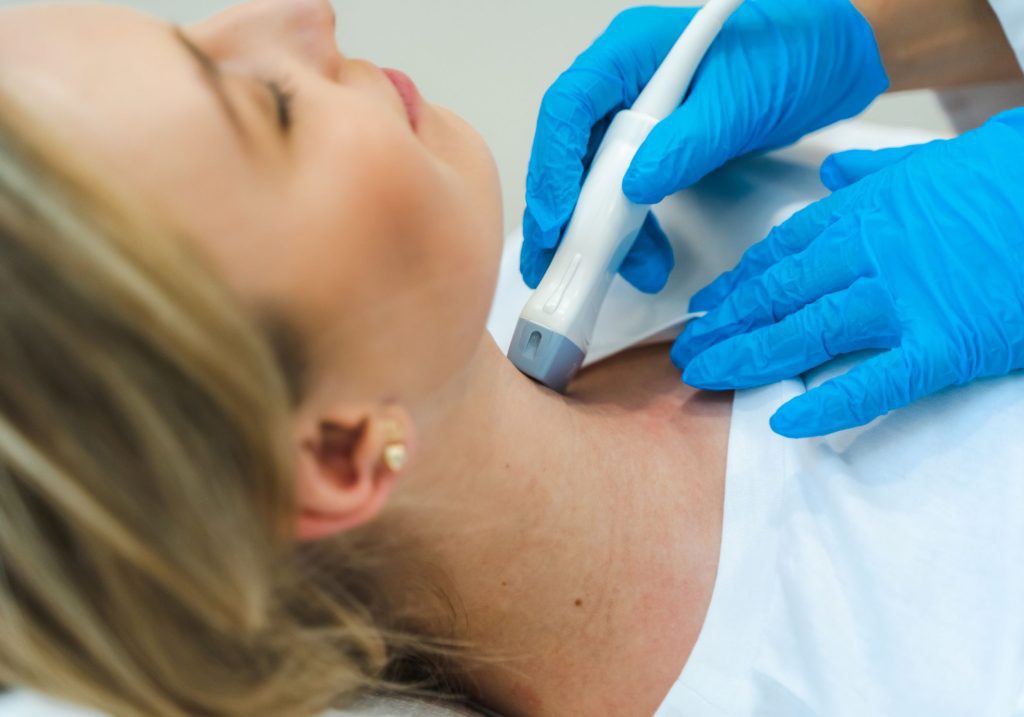 Lekarz Centrum Medycznego neoMedica w Poznaniu w rękawiczkach lekarskich przykłada głowicę USG do szyi kobiety